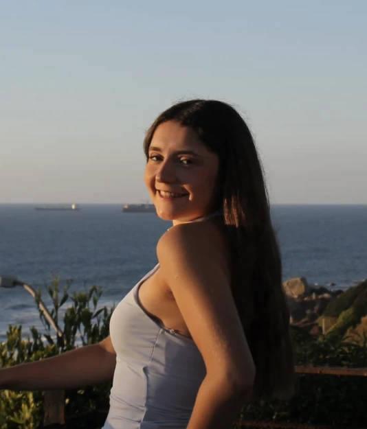 Fotografía de Emilia Zavala, exalumna destacada del preuniversitario, sonriendo al aire libre con vista al mar.